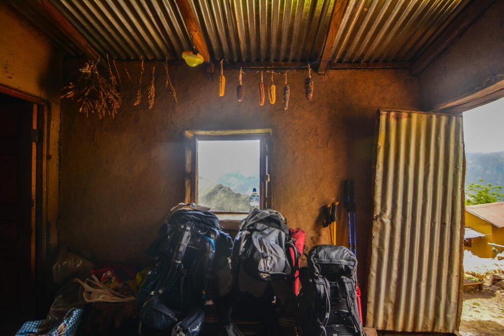 3 hiking bags sit on a bench underneath corn that is hanging to dry inside of a teahouse