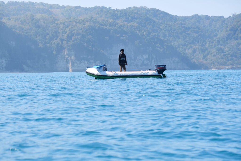 Man stands on small dinghy in the bay of Sumbawa away from the breaking waves