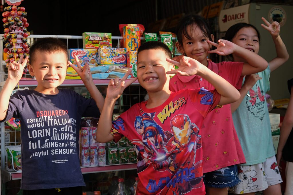 Four kids give peace signs to the camera in front of a small convenience store in Bac Son, Vietnam.