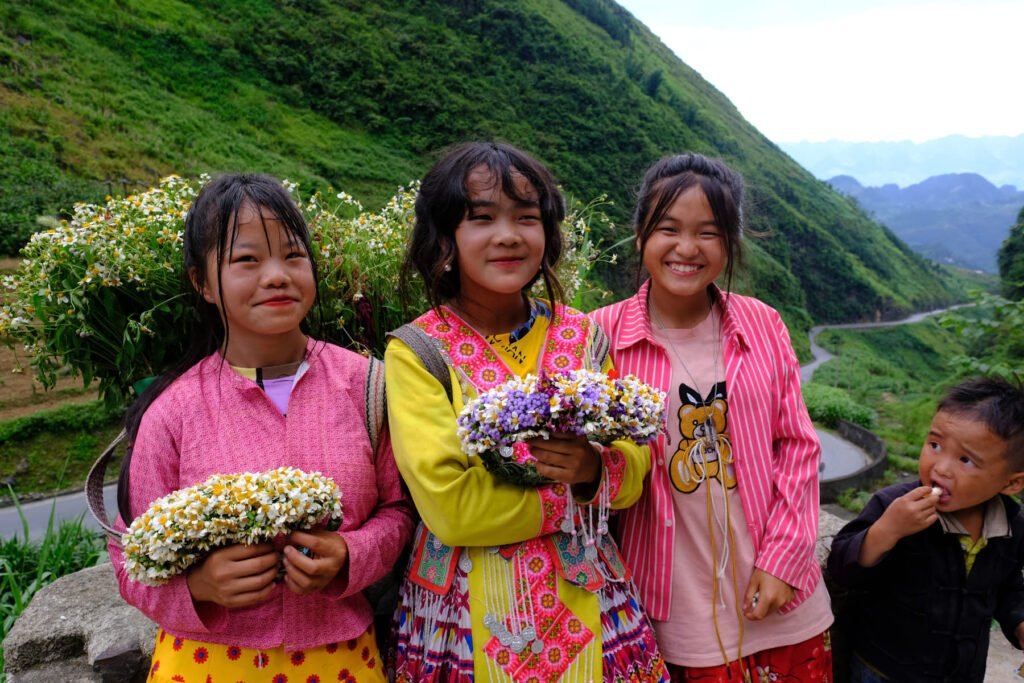 Three girls in pink traditional dress with flower bouquets, pose shyly in front of the camera. Doc Tham Ma, Vietnam.