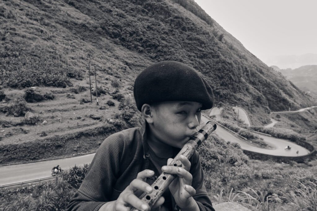 A young boy majestically plays the flute in front of a typical winding road in north Vietnam. Black & white photography.