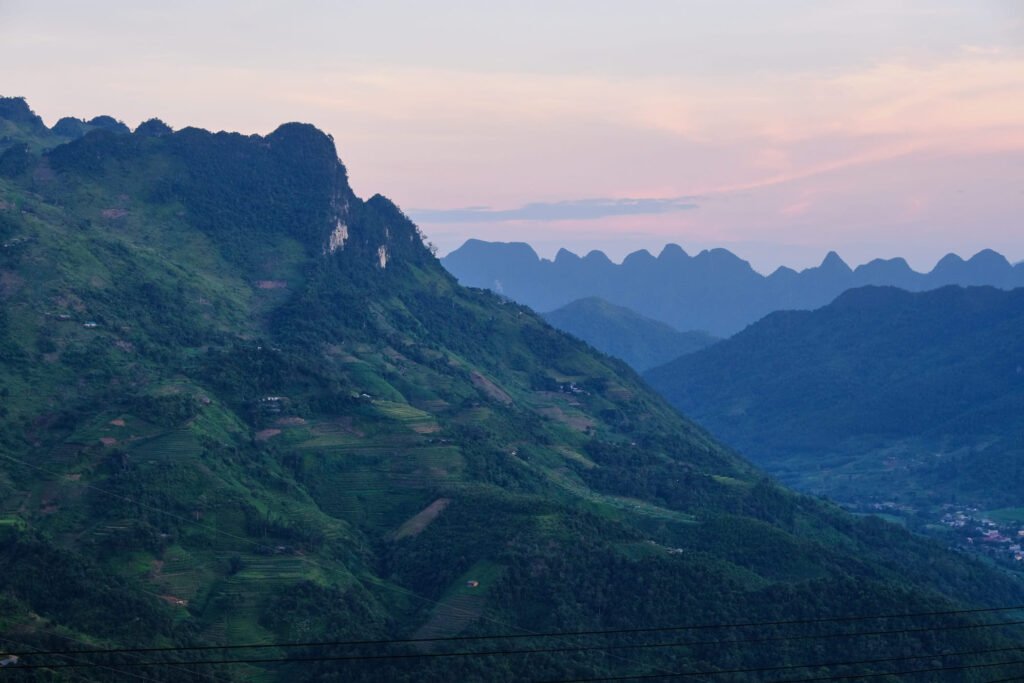 The light faes which leaves a soft pink and blue hue to the sky and far mountain ranges. The ranges dominate the landscape, which humans have somehow occupied with rice terraces scattered on the 'hills'.