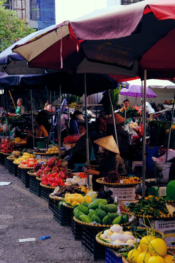 Fruit and vegetable vendors place their supplies in baskets on top of black trays, waiting under umbrellas to make their next sale