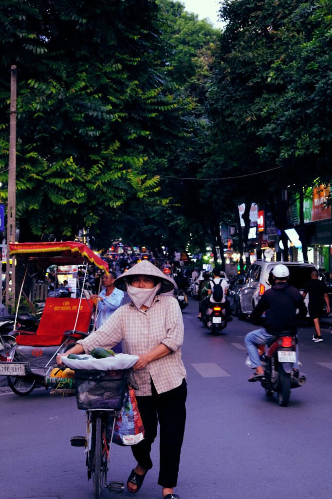 A woman walks her bicycle towards the camera, in the opposite direction of the flowing traffic.