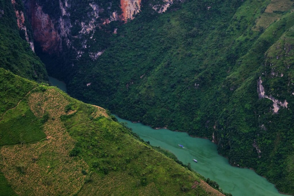 A unique angle of Tu San canyon from a vantage point near Ma Pi Leng sky path. The turquoise water contrasts against the green cliffs and red rock.