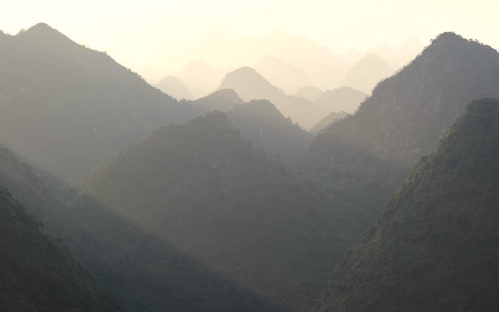 From Na Lay peak looking across the valley towards the endless layers of mountain ranges. The rising sun shines through the valley creating a layered hue of oranges which intensifies as the layers get further away.