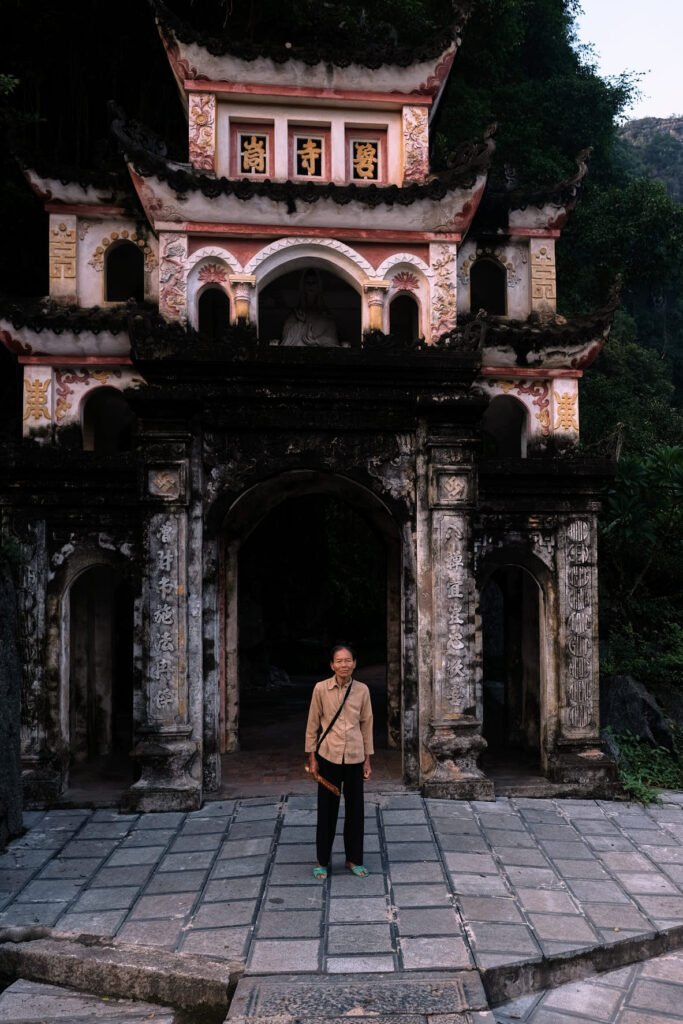 A woman stands in front of Bich Dong pagoda in Tam Coc. The pagoda is a classic Buddhist structure from ancient times.