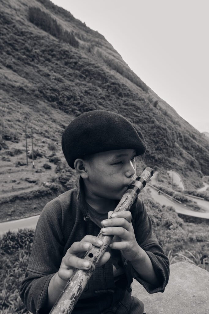 A young boy majestically plays the flute in front of a typical winding road in north Vietnam. Black & white photography.