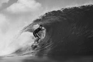 A black and white photograph, which provides a high contrast due to the light hitting the water at different angles. Local surfer scoring a beautiful barrel