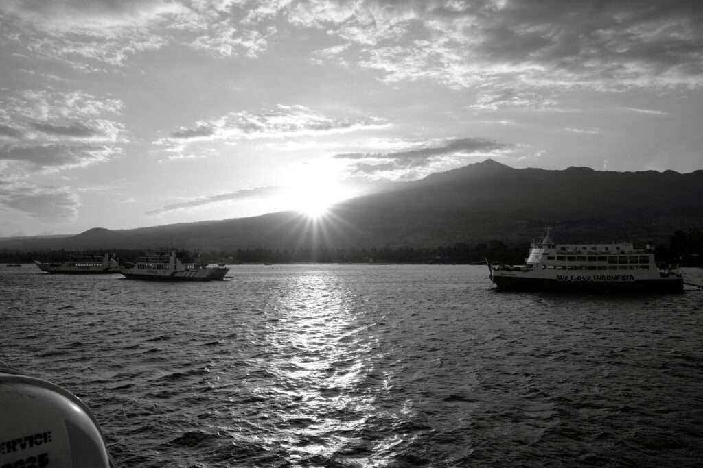 Ferries sit in the bay near the Kayangan ferry terminal in Lombok. A photographic technique 'sun star' completes the scene as the sun reflects on the surface of the water