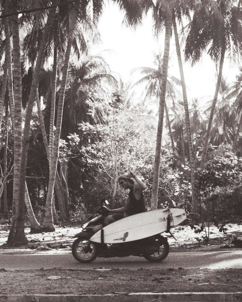 Driving through farmland with coconut trees overhead, surfboard in tow