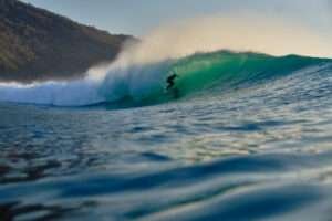 The setting sun backlights a barrel at Scar Reef. A surfer sits perfectly inside