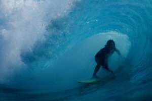 A surfer sits deep inside the barrel as the thick exploding blue lip curls over him